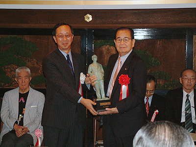 川越市長(右)とともにブロンズ像をかかげる宮崎市長