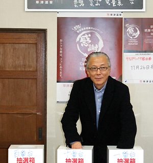 抽選箱に手を入れ選ぶ市川旅組理事長