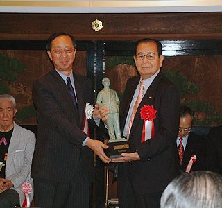 川越市長(右)とともにブロンズ像をかかげる宮崎市長